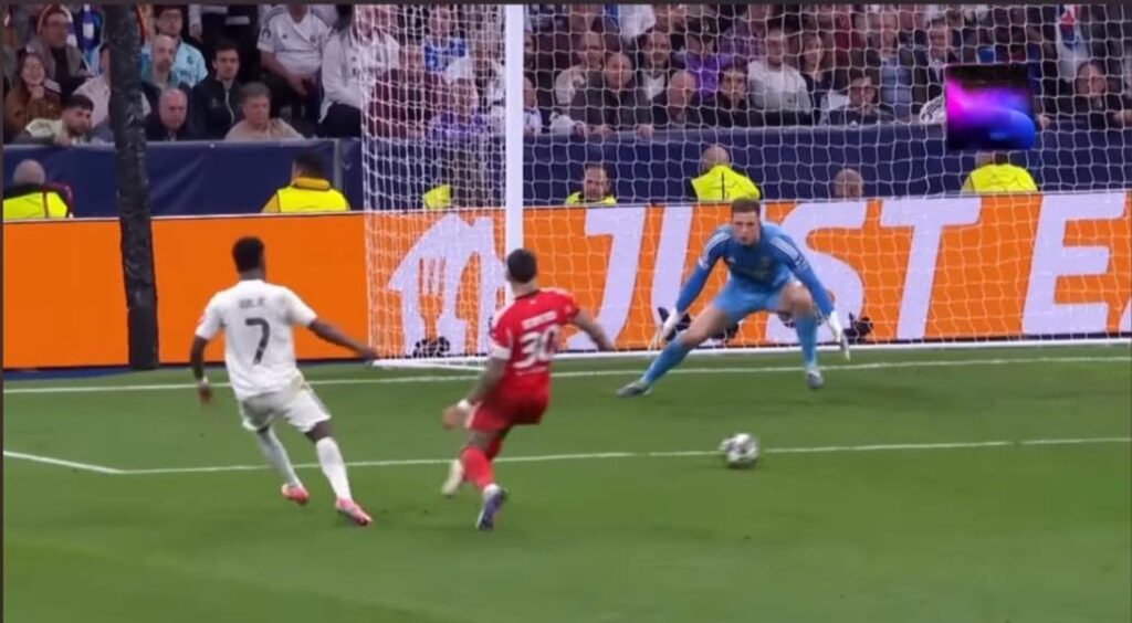 Vinicius Junior celebrating his decisive goal for Real Madrid in a UEFA Champions League knockout match against Benfica, with teammates cheering around him in a packed Santiago Bernabéu Stadium under bright lights.